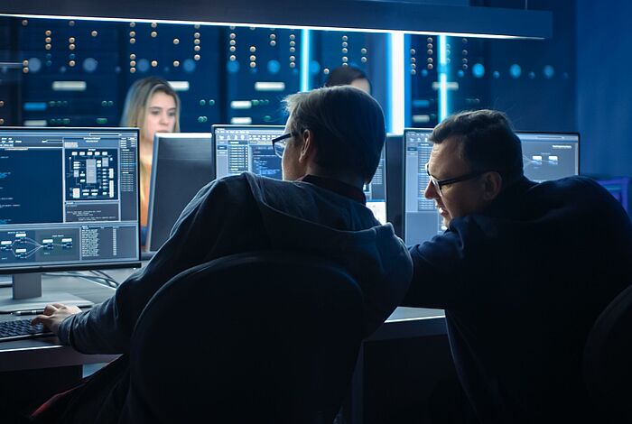 Pentest einer Software Zwei Männer sitzen vor Monitoren mit Code