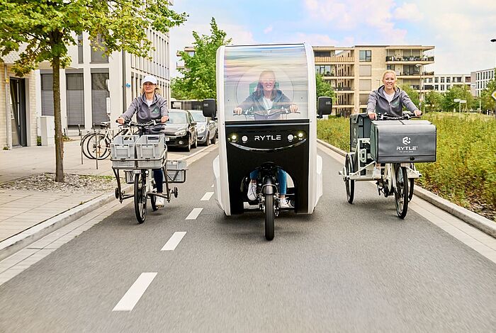 Drei verschiedene RYTLE E-Cargo-Bikes fahren auf einer Straße